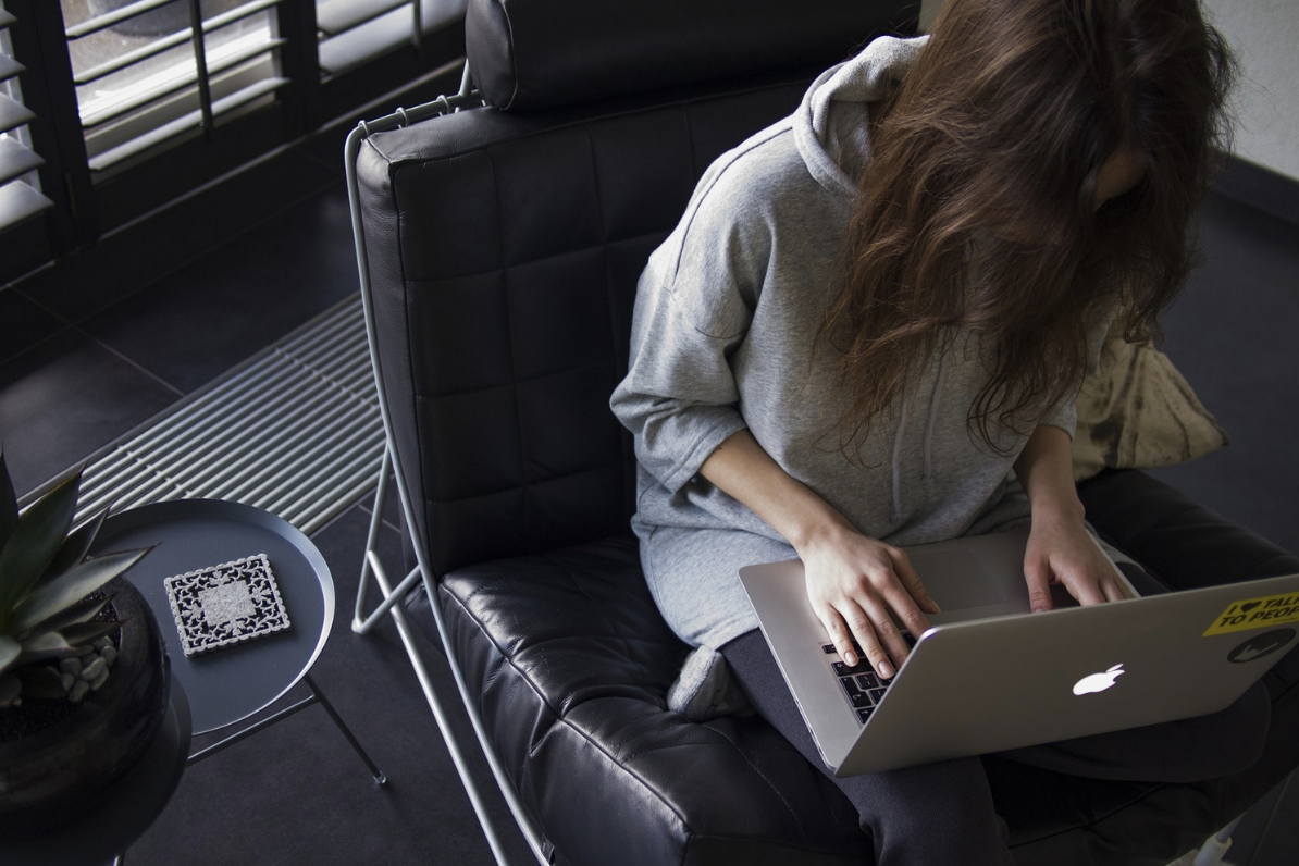 Woman in long-sleeved top sitting on black leather chair with silver MacBook on her lap